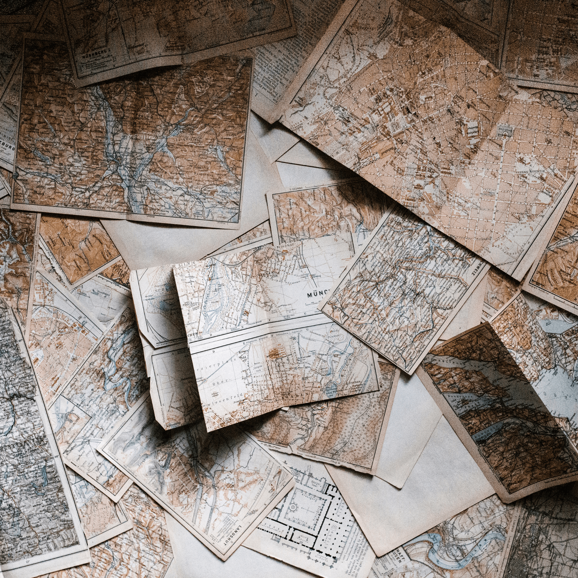 A collection of antique maps and historical cartography documents spread across a table, showcasing detailed geographic and city layouts.